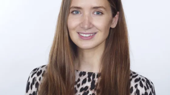 A woman with long brown hair smiling at the camera, wearing a leopard print top.