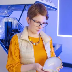 Photo of Laura standing in front of a microscope and holding a bivalve shell
