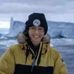 Picture of person in front of an iceberg wearing a beanie and yellow jacket