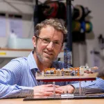 Ron Hackney posing behind a model of scientific drilling vessel Chikyu